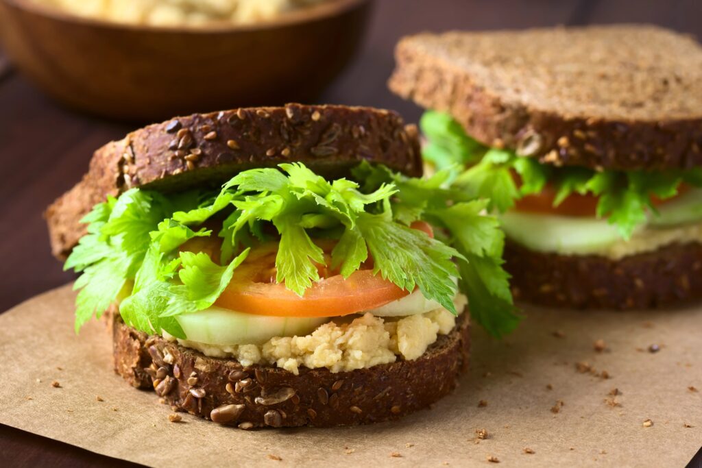 Volkoren sandwiches gevuld met geprakte kikkererwtensalade, tomaat, komkommer en bladselderij