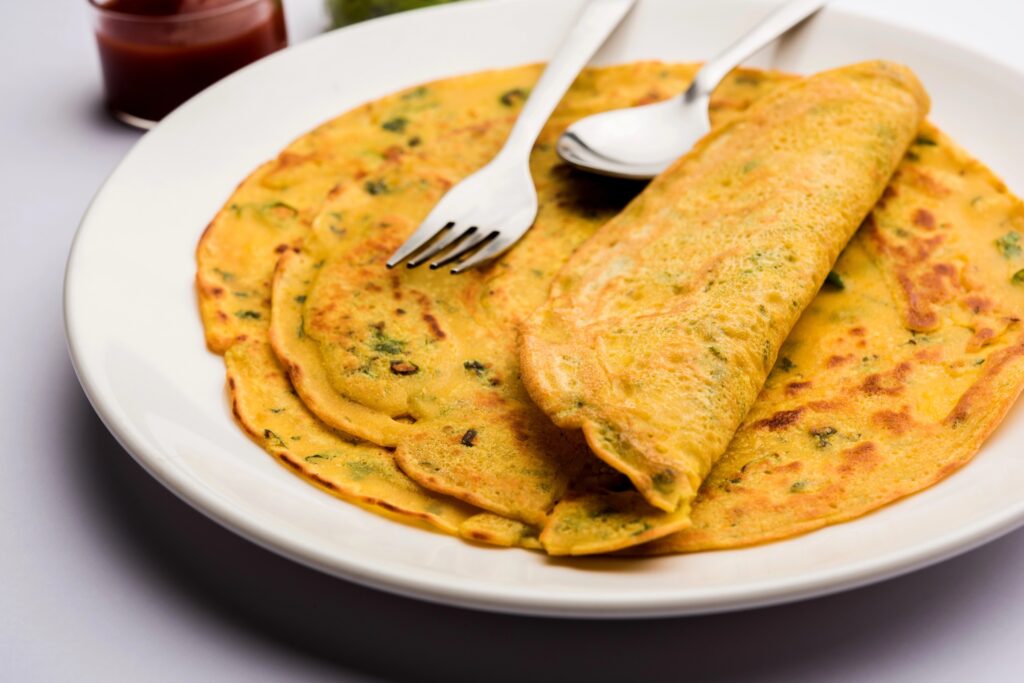 Bord met opgerolde kikkererwtenmeel-omeletten (besan chilla) met verse kruiden, met bestek en een potje chutney ernaast