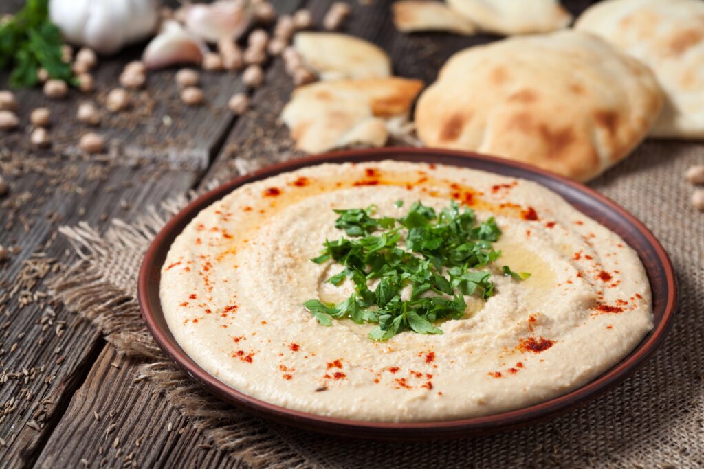 Schaal romige zelfgemaakte hummus met peterselie, paprikapoeder en olijfolie, met platbrood en kikkererwten op een houten tafel