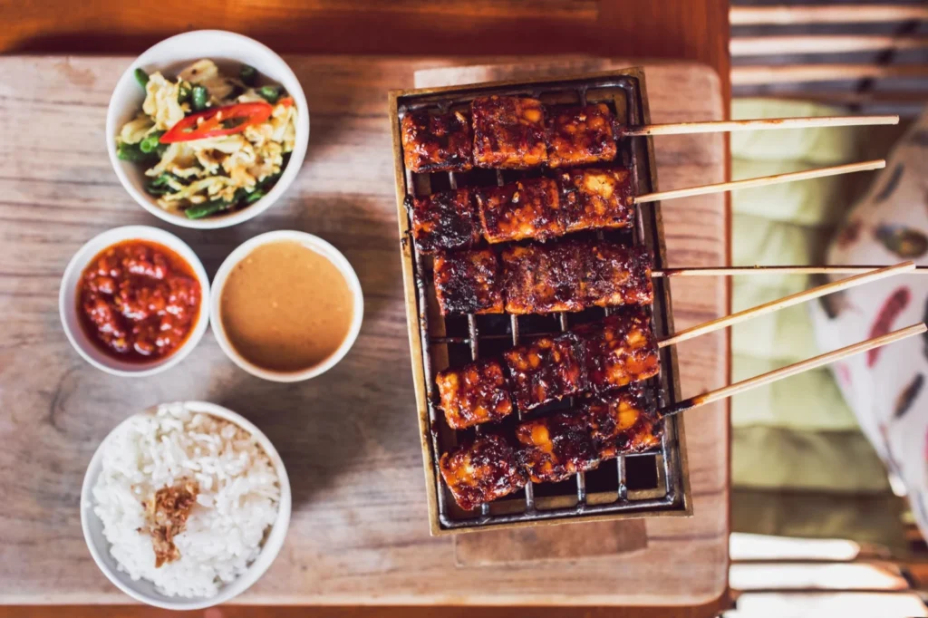 Gegrilde seitan-saté op spiesjes met satesaus en gebakken uitjes